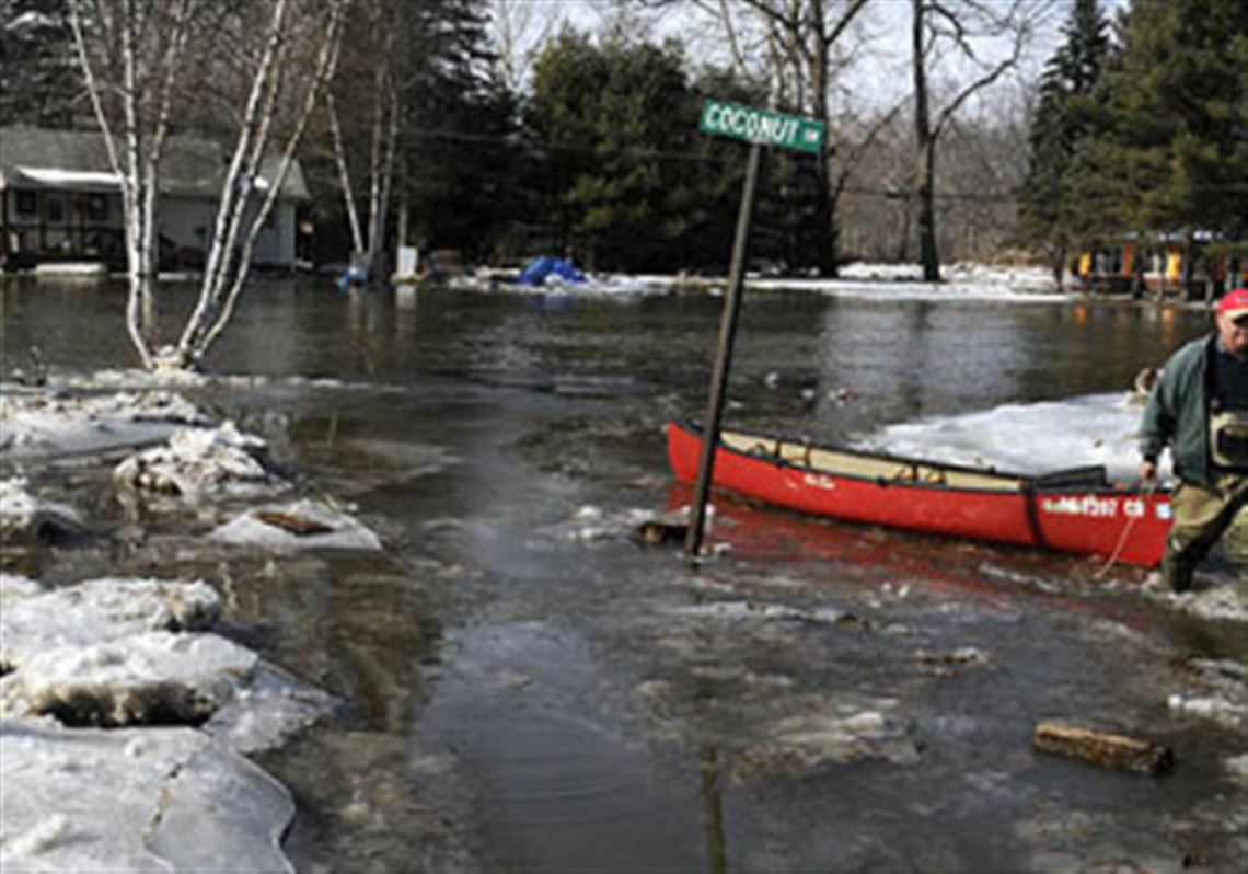 Dave Porada pulls his canoe across the Neshannock Creek near a flooded Coconut Drive. Porada said the basement of his house, upper left, is flooded.