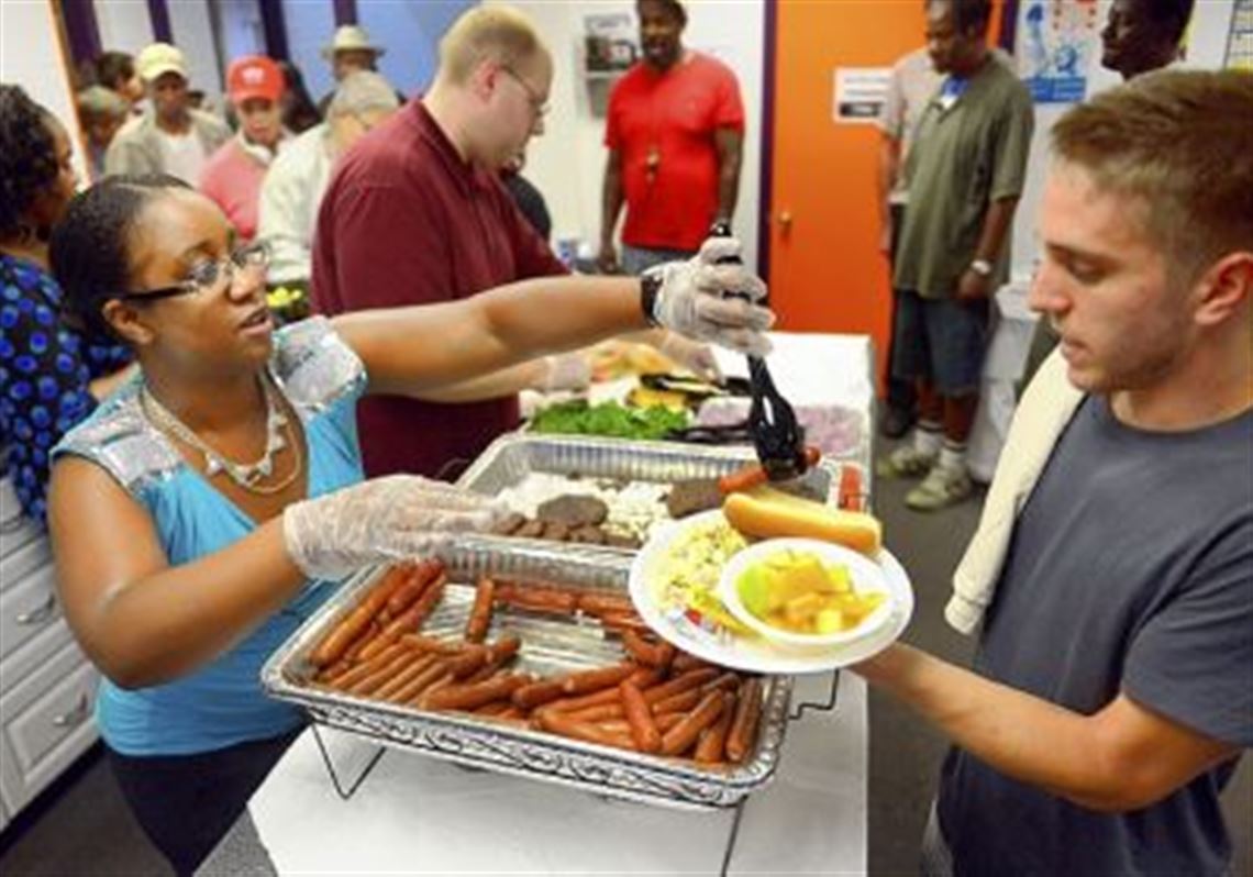 Shaunte Blanchard, a case manager for the supportive housing program at Community Human Services, serves a hot dog to University of Pittsburgh senior Evan Arnet during their Oakcliffe community cookout at the CHS Community Center on Wednesday.