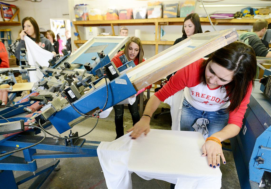 Freedom Area High School student Sydney Kaercher helps set up the printer for a T-shirt run at RooTees silk screen printers.
