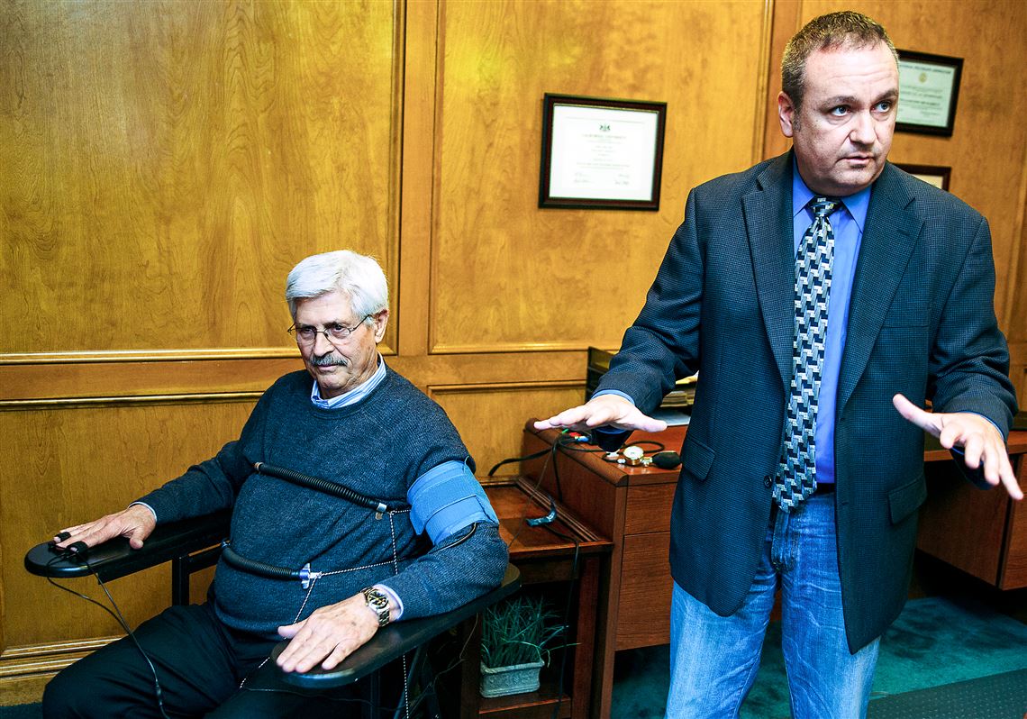 Bill Barrett of Assured Polygraph Services Inc. demonstrates polygraph equipment on his colleague Morris Ragus, seated, a retired polygraph examiner. 
