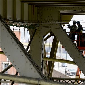 Workers weave a web of cables to support protective canvas and nets under the Liberty Bridge Wednesday. A major refurbishment of the bridge is beginning.