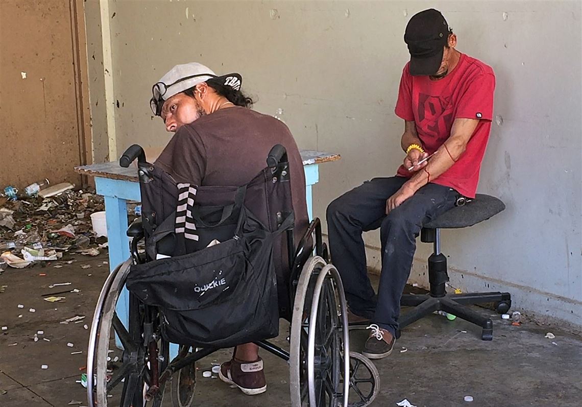 Carlos Perrios, right, injects himself with drugs as Oliver Franco Rivero looks over his shoulder while sitting in a shooting den at an abandoned school in Cidra, Puerto Rico, on October 19, 2017.
