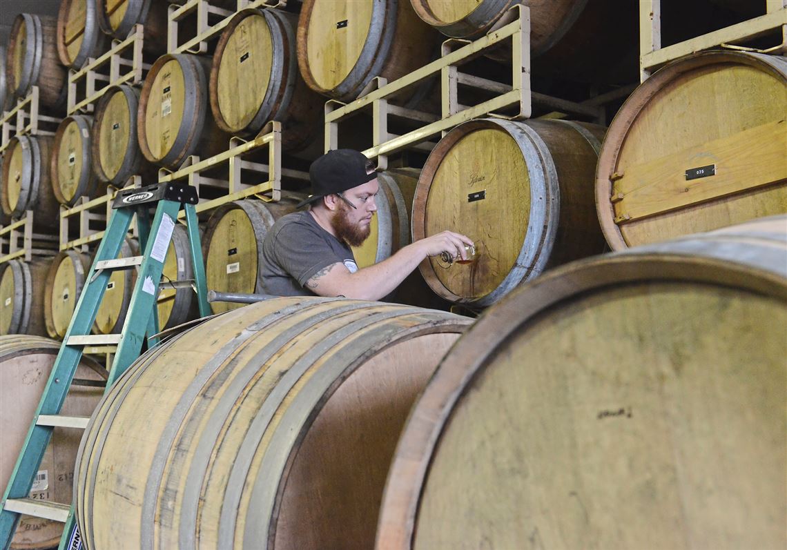 Bert Mooney IV checks beer aging in the rack of barrels at Strange Root Experimental Ales in West Deer.  