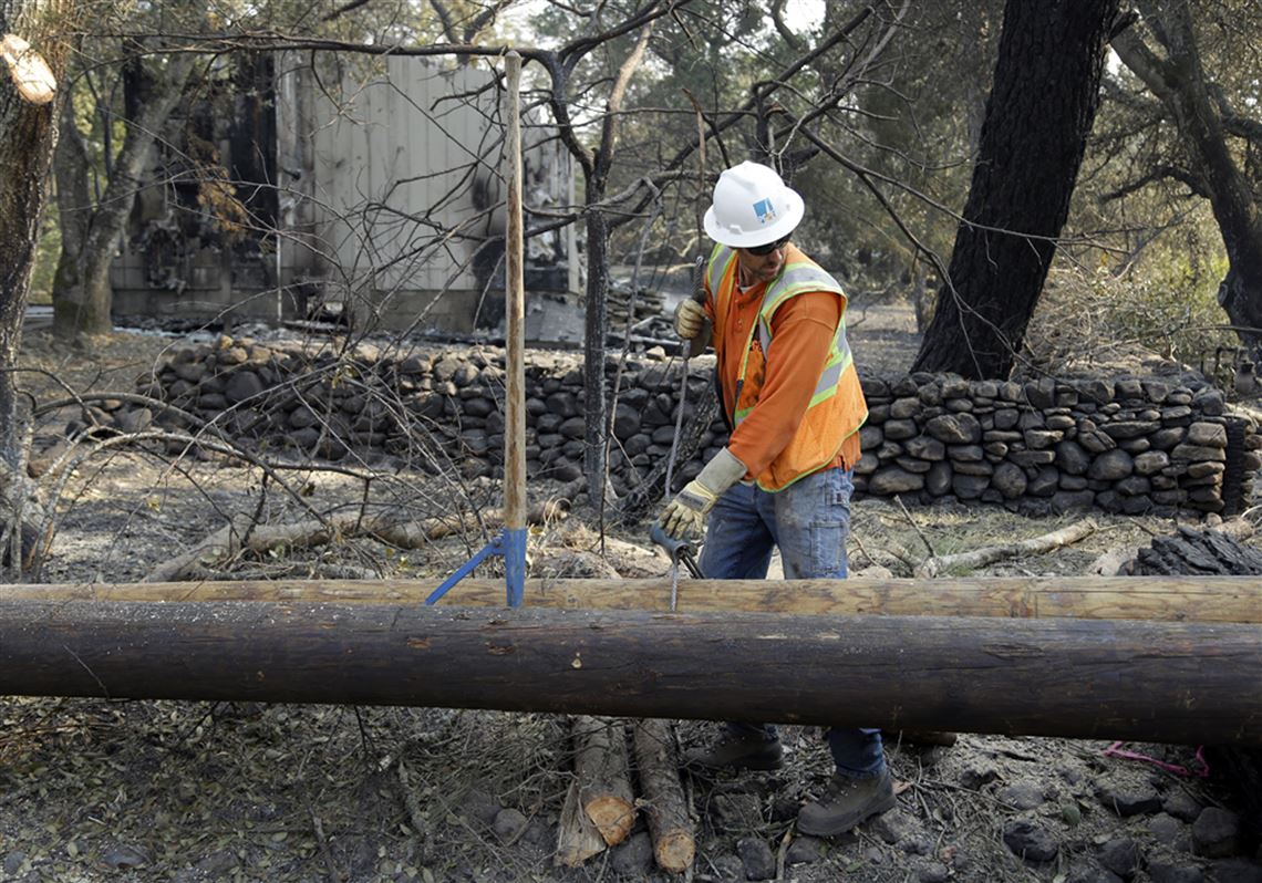 FILE - In this Oct. 18, 2017 file photo, a Pacific Gas & Electric worker replaces power poles destroyed by wildfires in Glen Ellen, Calif. California fire officials say sagging PG&E power lines that made contact ignited a blaze last year in California that killed four people and injured a firefighter. The California Department of Forestry and Fire Protection said Tuesday, Oct. 9, 2018 that strong winds caused the lines to come into contact and send molten material onto dry vegetation in Yuba County. It was one of several wildfires that swept through Northern California that month, killing 44 people. (AP Photo/Ben Margot, file)