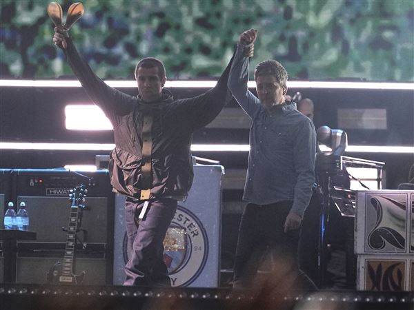 Liam Gallagher, left, holds the hand aloft of Noel Gallagher from the band Oasis as they perform Friday during their reunion concert in Cardiff, Wales.