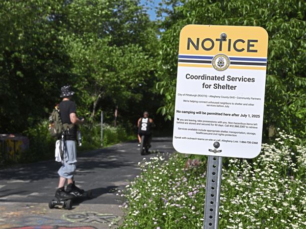 Trail users pass a City of Pittsburgh sign cautioning that camping will be prohibited along the Three Rivers Heritage Trail on the South Side on Wednesday, June 11, 2025. A number of homeless encampment tents remain setup along the trail between the Color Park and the Southside Works.    
